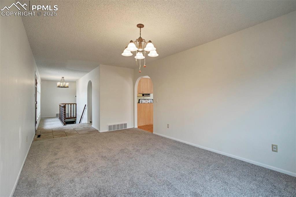 Image 13 of 45: Family room featuring a chandelier, a textured ceiling, carpet, arched walk