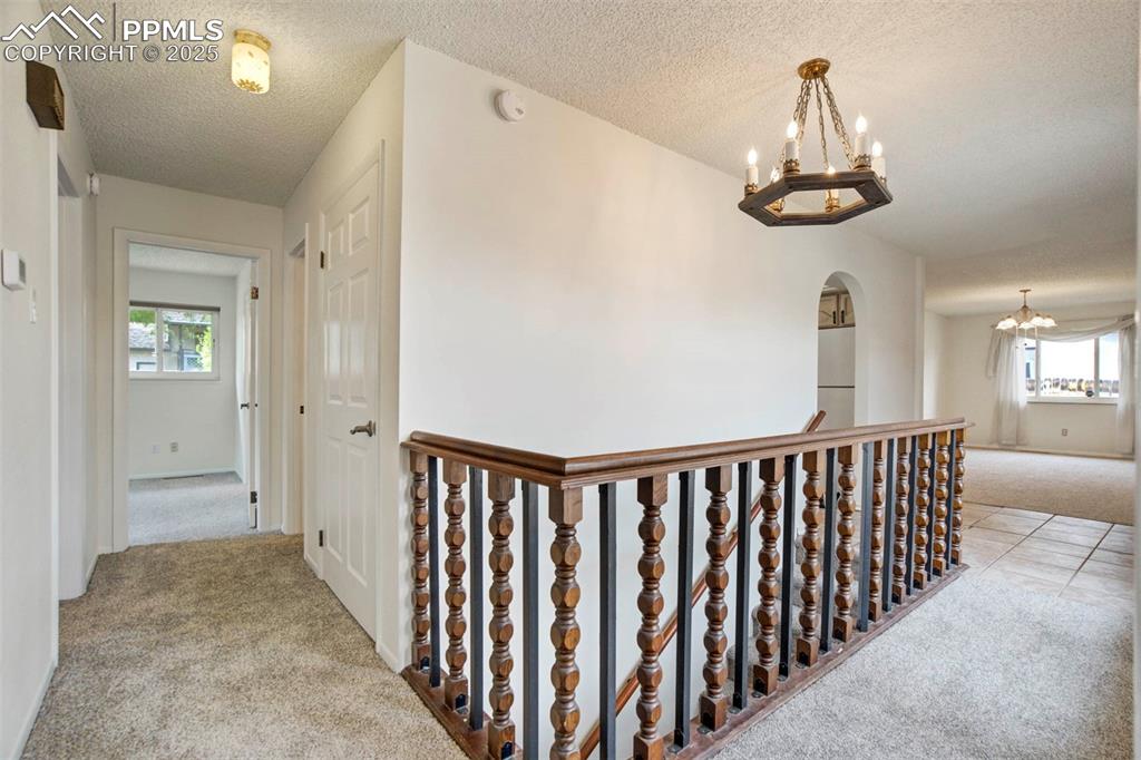 Image 14 of 45: Corridor featuring light colored carpet, a chandelier, an upstairs landing,