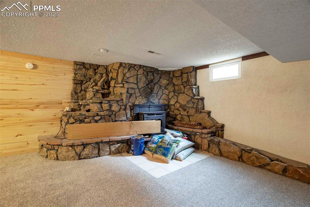 Image 33 of 45: Basement Great Room with a wood stove, carpet flooring, a textured ceiling,