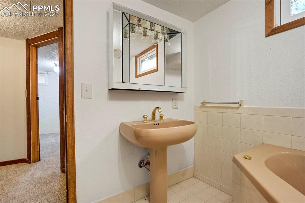 Image 38 of 45: Bathroom with a textured ceiling, light tile patterned floors, tile walls, 