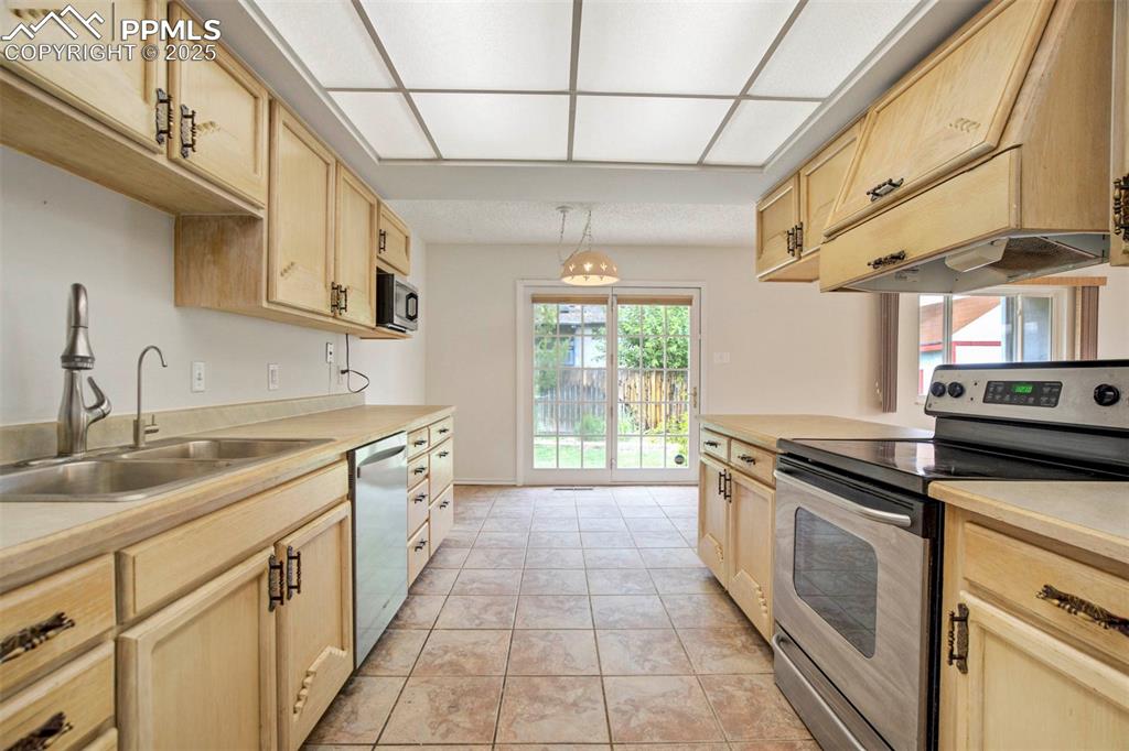 Image 9 of 45: Kitchen with light brown cabinetry, stainless steel appliances, light count