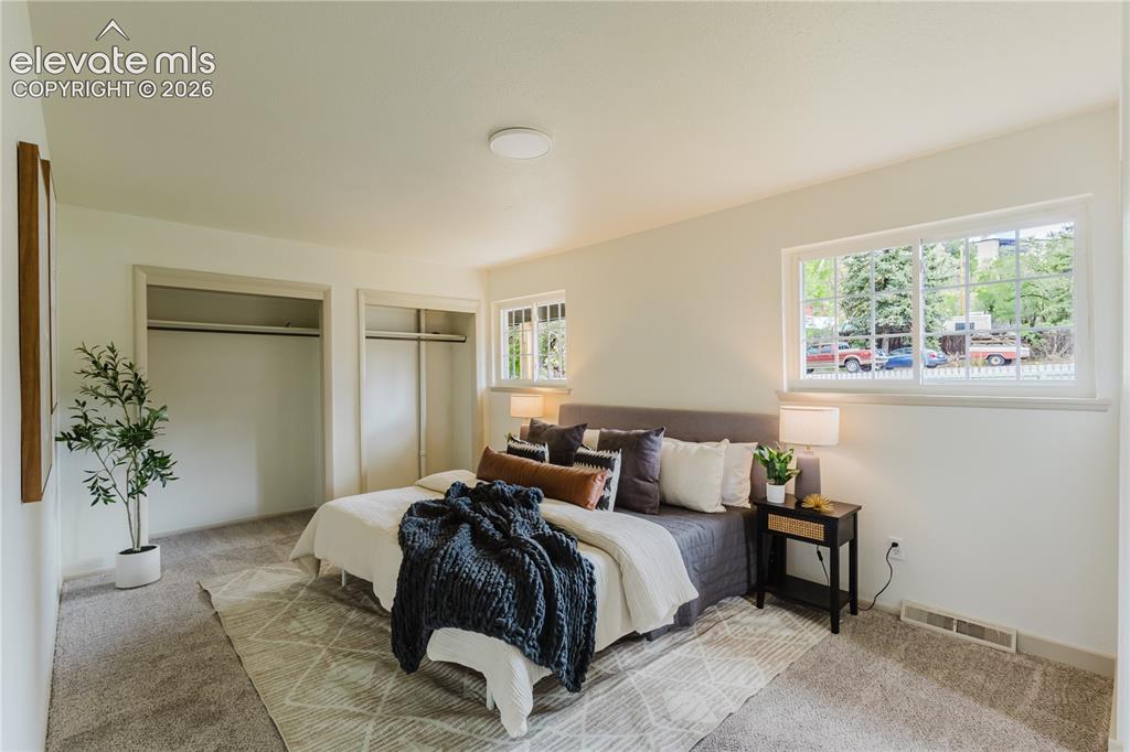 Image 14 of 47: Bright bedroom featuring neutral-toned carpet, white walls, and a large win