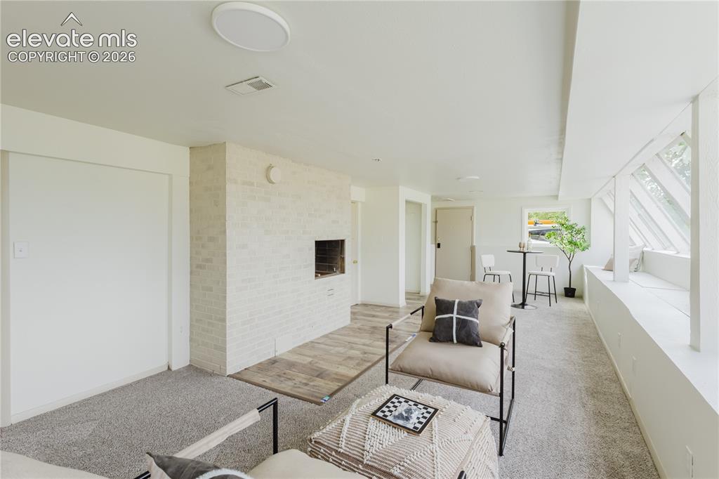 Image 28 of 47: Living area featuring a white-painted brick fireplace with a wood-finish he