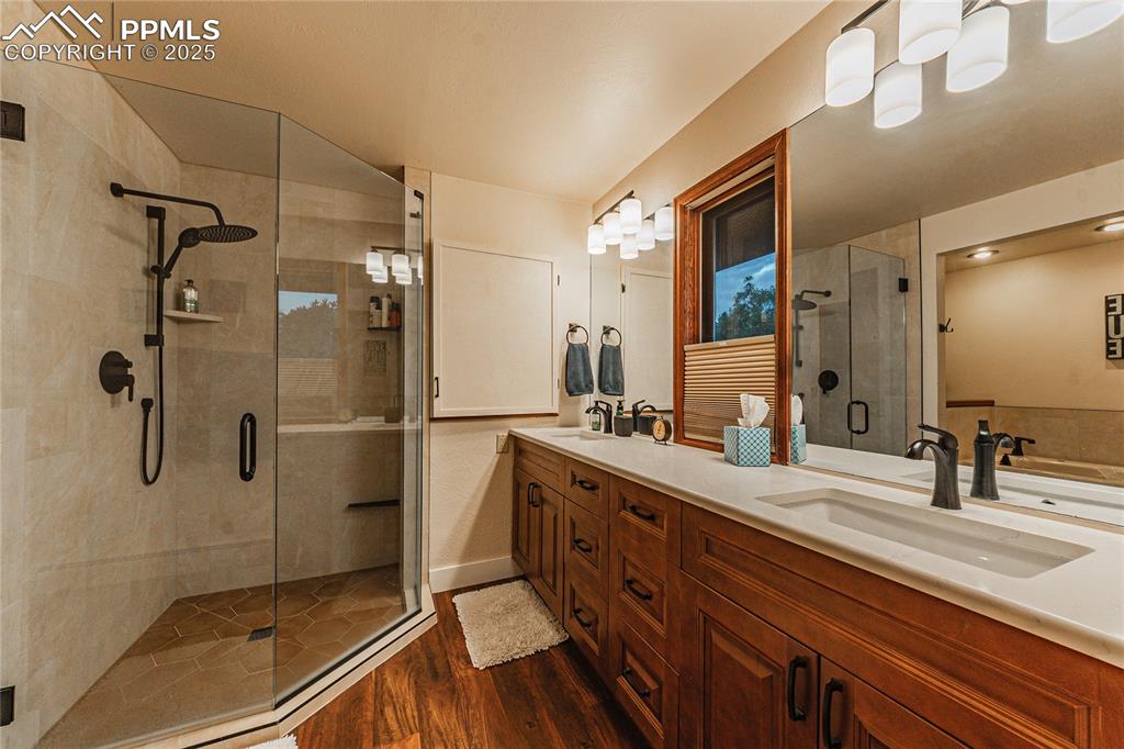 Image 16 of 39: Full bathroom with a stall shower, wood finished floors, double vanity, and