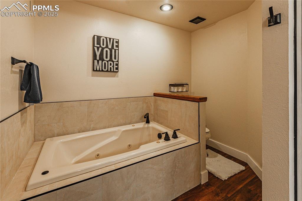 Image 18 of 39: Full bathroom with toilet, wood finished floors, a whirlpool tub, and baseb