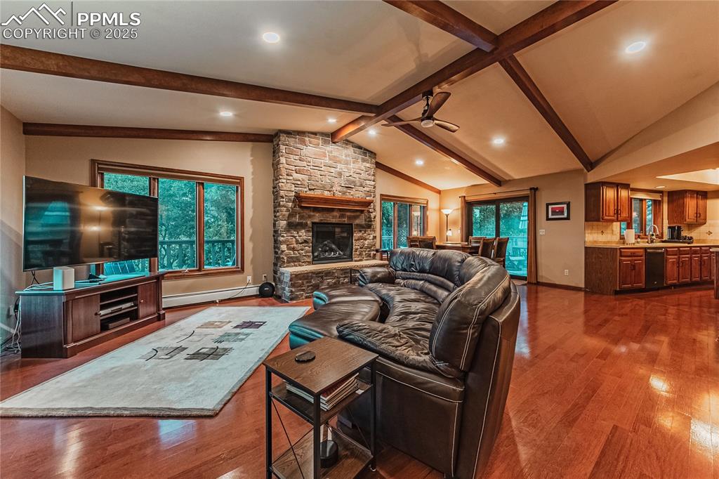 Image 4 of 39: Living area with baseboard heating, ceiling fan, a stone fireplace, dark wo