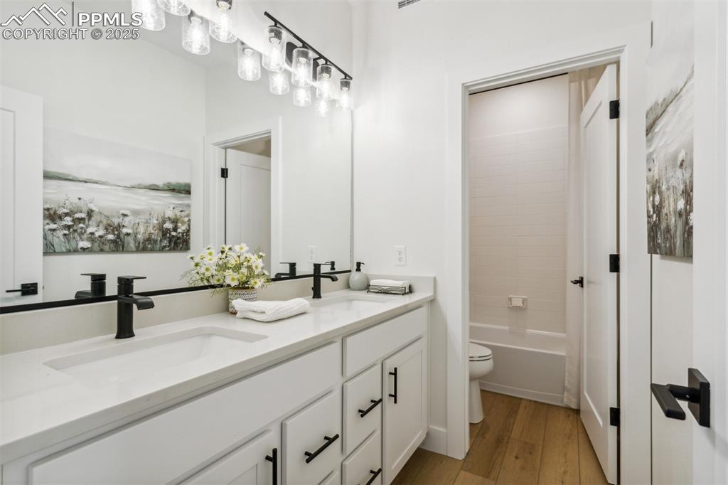 Image 16 of 23: Full bathroom with toilet, wood finished floors, double vanity, and a sink