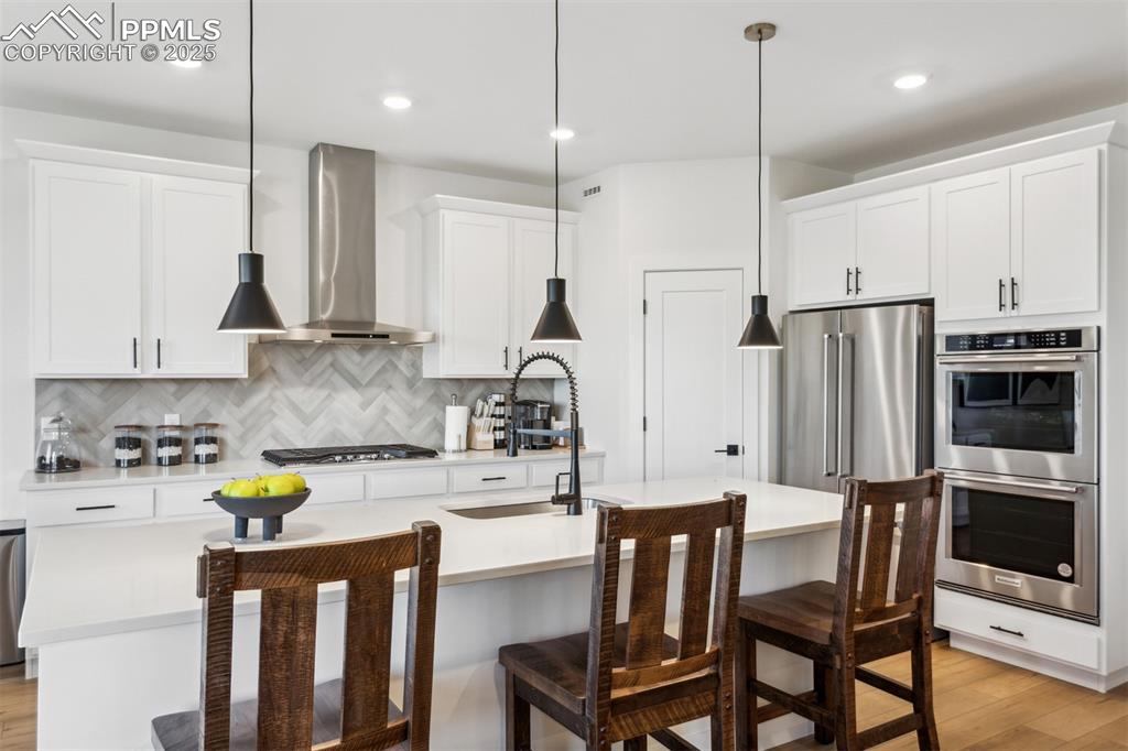 Image 2 of 23: Kitchen featuring wall chimney range hood, light countertops, light wood-ty