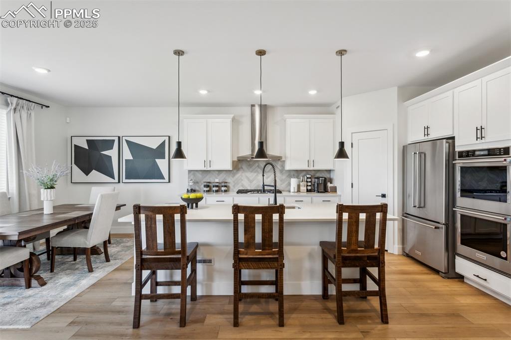 Image 6 of 23: Kitchen with tasteful backsplash, wall chimney exhaust hood, light countert