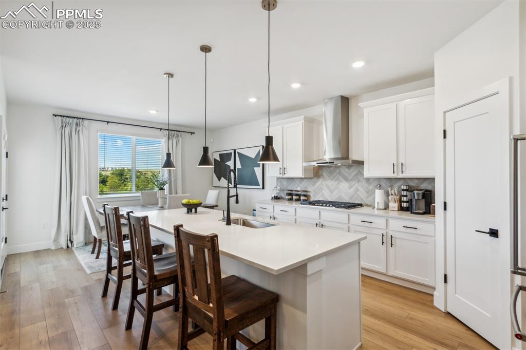 Image 8 of 23: Kitchen featuring wall chimney range hood, light countertops, backsplash, a