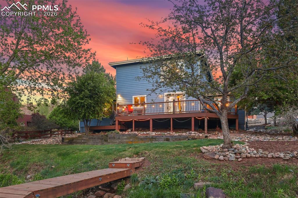 Image 8 of 47: Twilight photos of back of structure featuring bridge over backyard creek
