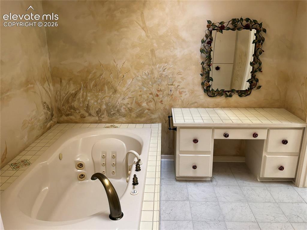 Image 18 of 21: Built-in jetted tub with brass fixtures and tiled surround