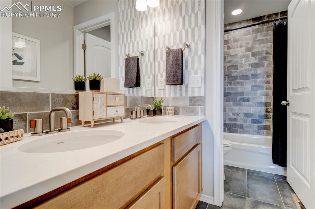 Image 18 of 25: Full bath with double vanity, shower / bathtub combination with curtain, an