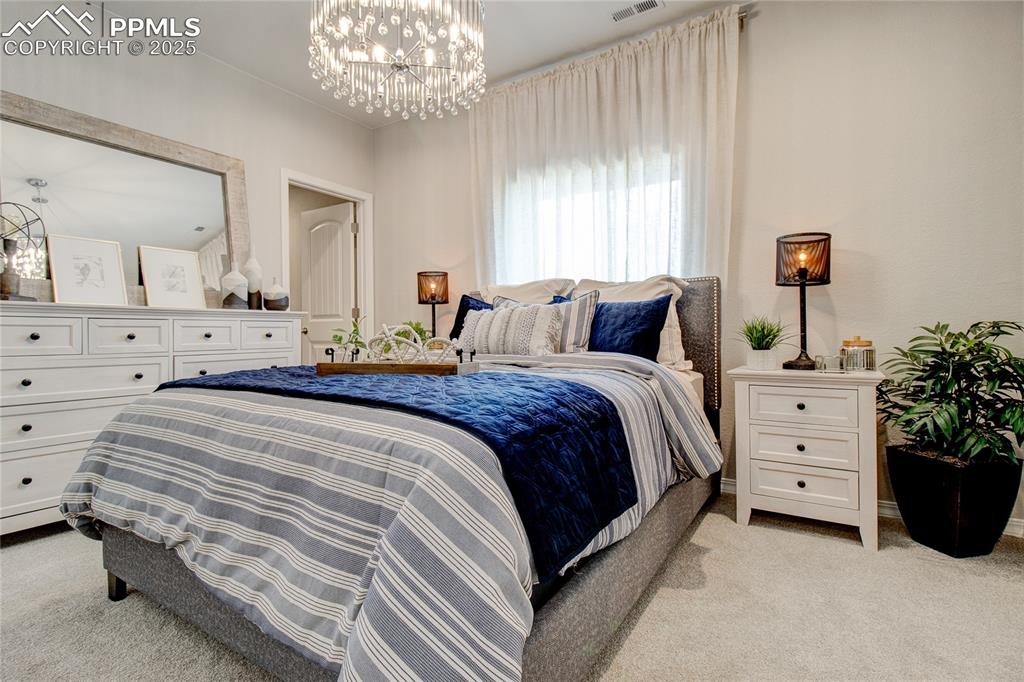 Image 24 of 25: Bedroom with a chandelier and light colored carpet