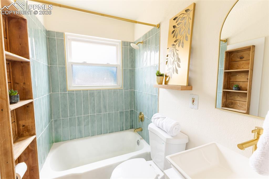 Image 19 of 24: Bathroom featuring a white bathtub, light teal subway tile surround, and go