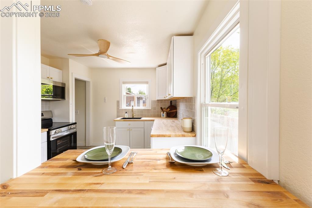 Image 8 of 24: Kitchen featuring butcher block countertops, white cabinetry, a tile backsp