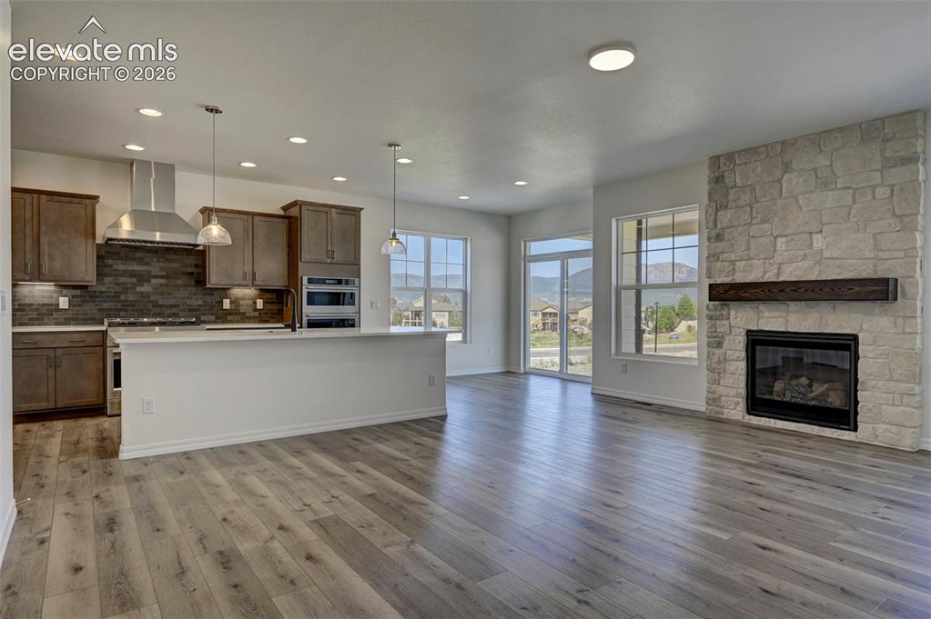 Image 15 of 35: gas fireplace with stonework to ceiling and wood mantel; kitchen with islan