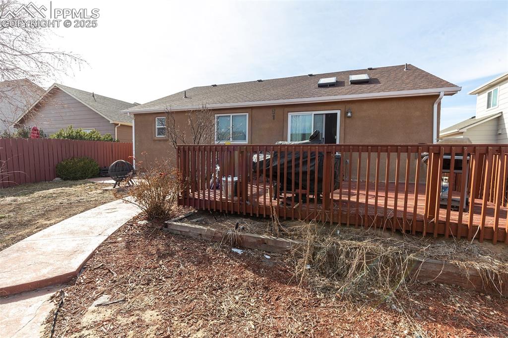 Image 10 of 12: Back of house featuring roof with shingles, stucco siding, fence, and a woo