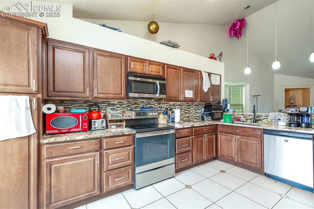 Image 3 of 12: Kitchen featuring vaulted ceiling, stainless steel appliances, decorative b