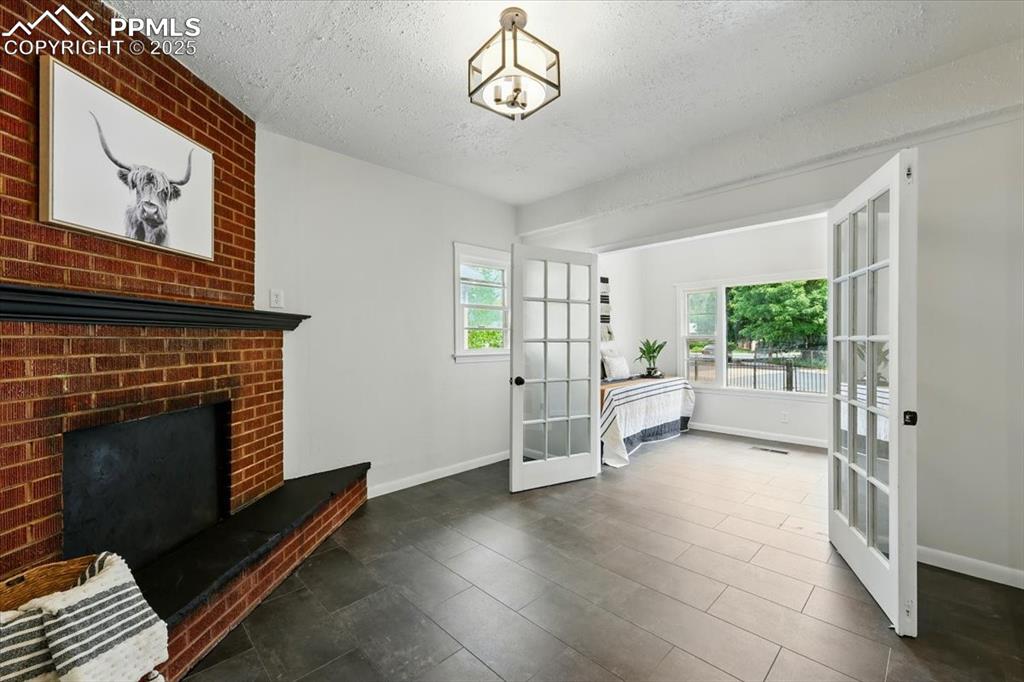 Image 10 of 32: Unfurnished living room with french doors, a textured ceiling, a brick fire