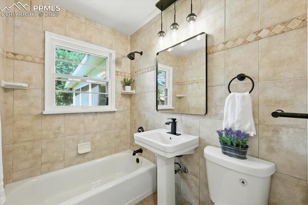 Image 18 of 32: Bathroom featuring plenty of natural light, tile walls, and tub / shower co