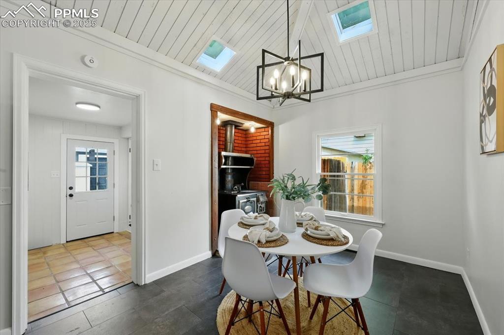 Image 25 of 32: Dining area featuring a skylight, a wood stove, a chandelier, wooden ceilin