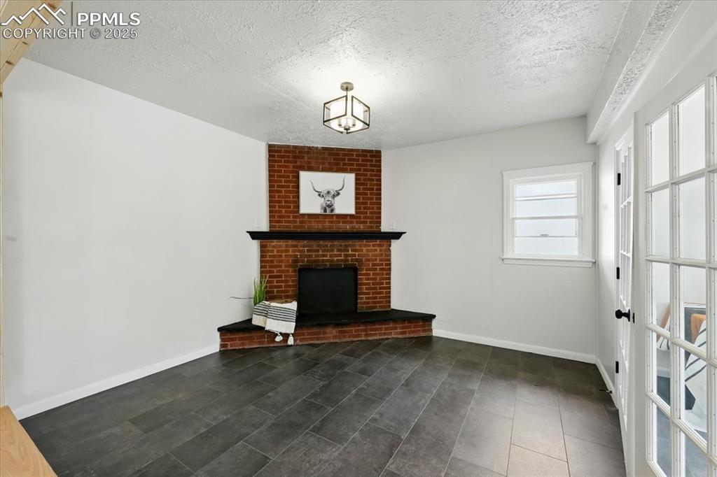 Image 8 of 32: Unfurnished living room with a textured ceiling and a brick fireplace