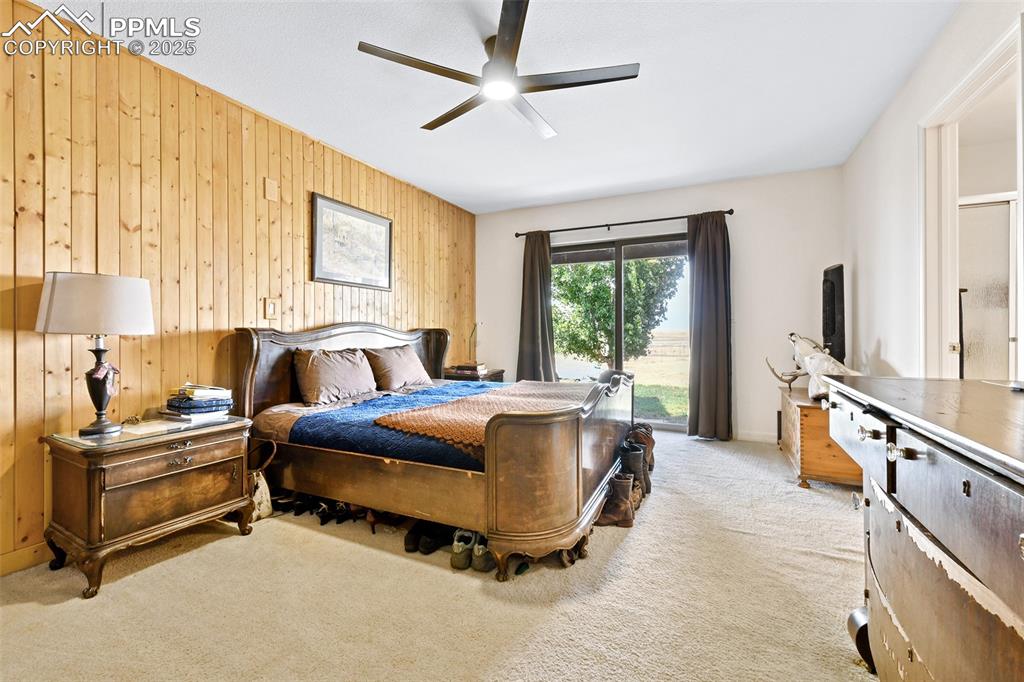 Image 10 of 22: Bedroom featuring wood walls, light colored carpet, ceiling fan, and access