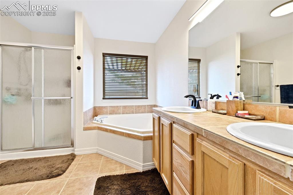 Image 13 of 22: Bathroom featuring a bath, a shower stall, double vanity, and light tile pa
