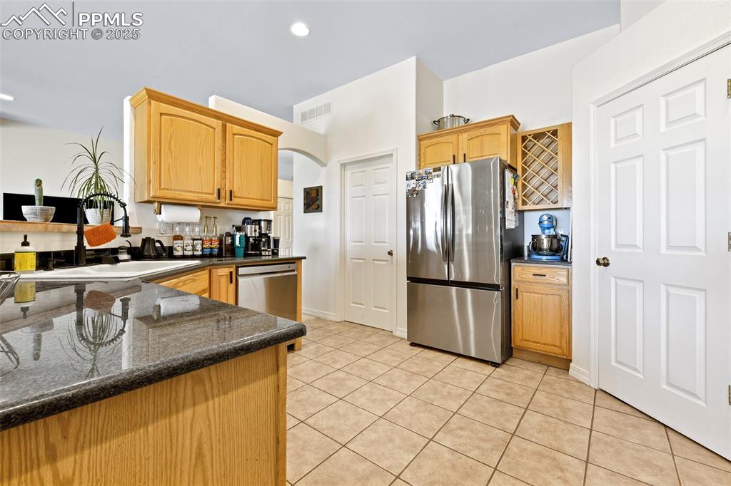 Image 7 of 22: Kitchen with stainless steel appliances, dark stone countertops, light tile