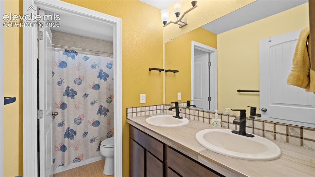 Image 22 of 45: Dual vanity with undermount sinks, bronze faucets, and a tile backsplash