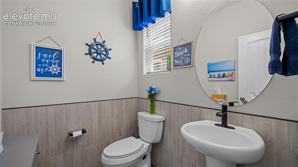 Image 6 of 45: Pedestal sink with a matte black faucet, oval mirror, and tile wainscoting