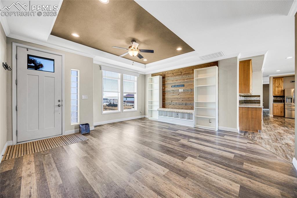 Image 12 of 50: Unfurnished living room with ceiling fan, crown molding, wood finished floo