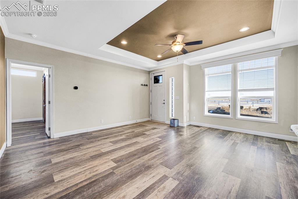 Image 46 of 50: Unfurnished living room featuring crown molding, a tray ceiling, ceiling fa