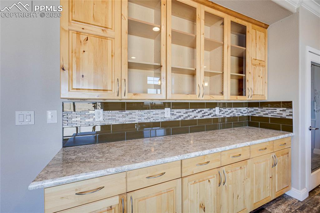 Image 8 of 50: Kitchen with light brown cabinetry, glass insert cabinets, and backsplash