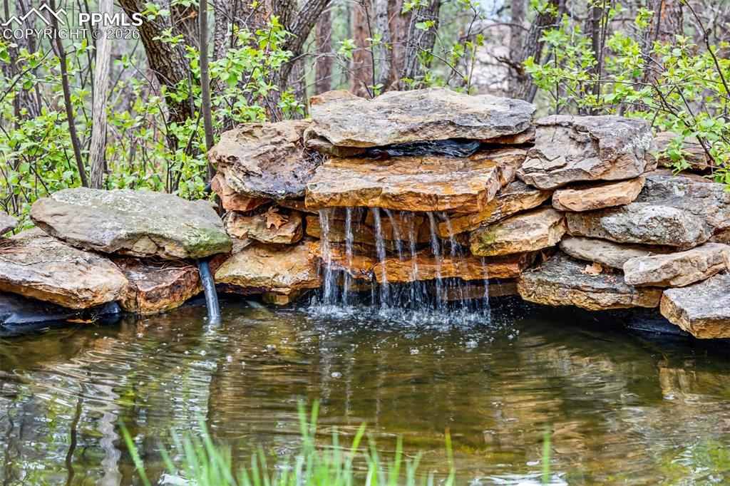 Image 38 of 44: A natural stone waterfall trickles gently beside the patio seating area, it