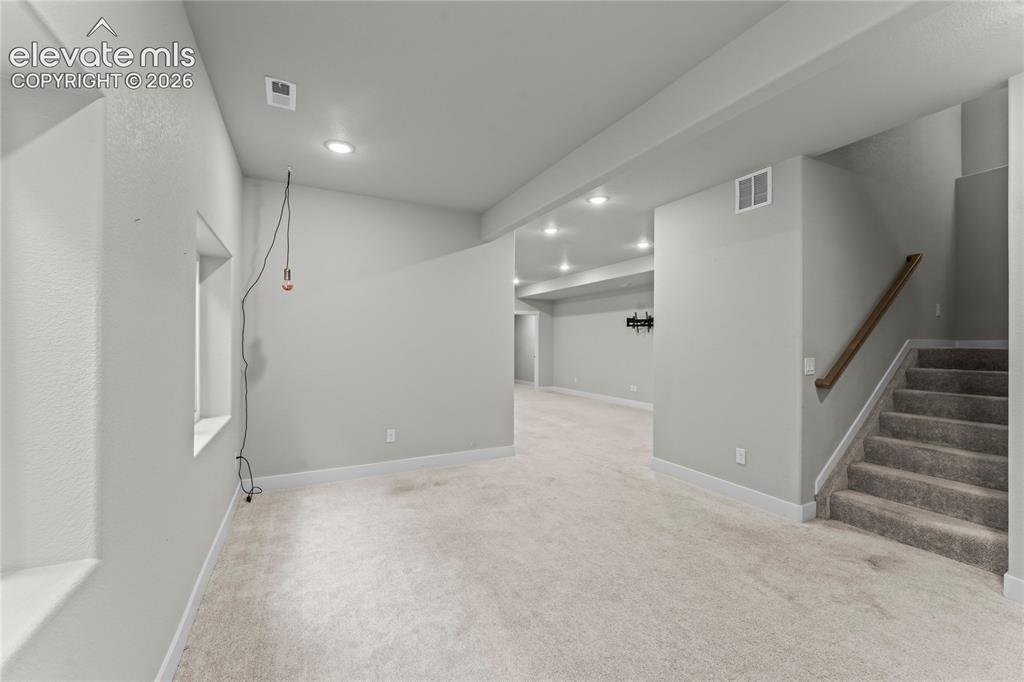 Image 13 of 17: Expansive carpeted area with recessed lighting, a window, and a staircase f