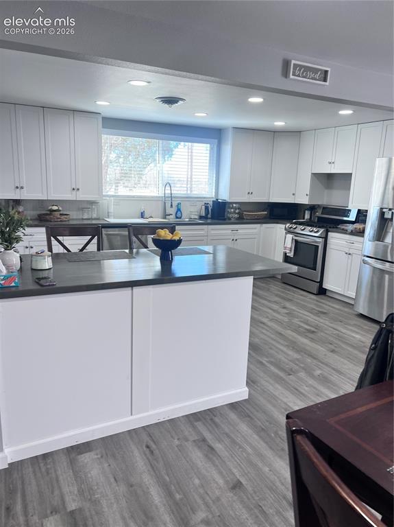 Image 23 of 49: White cabinetry, dark countertops, a center island, wood-finish flooring, a