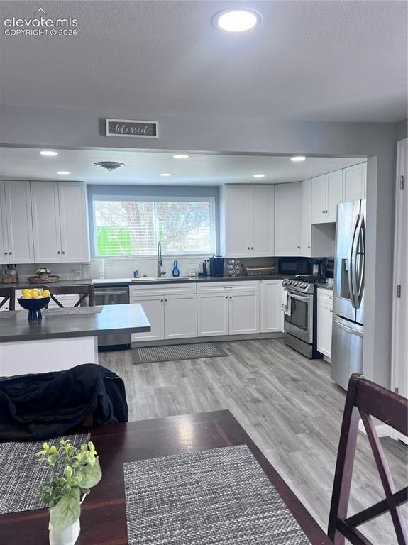 Image 24 of 49: Modern kitchen featuring wood-finish flooring, white cabinetry, dark counte