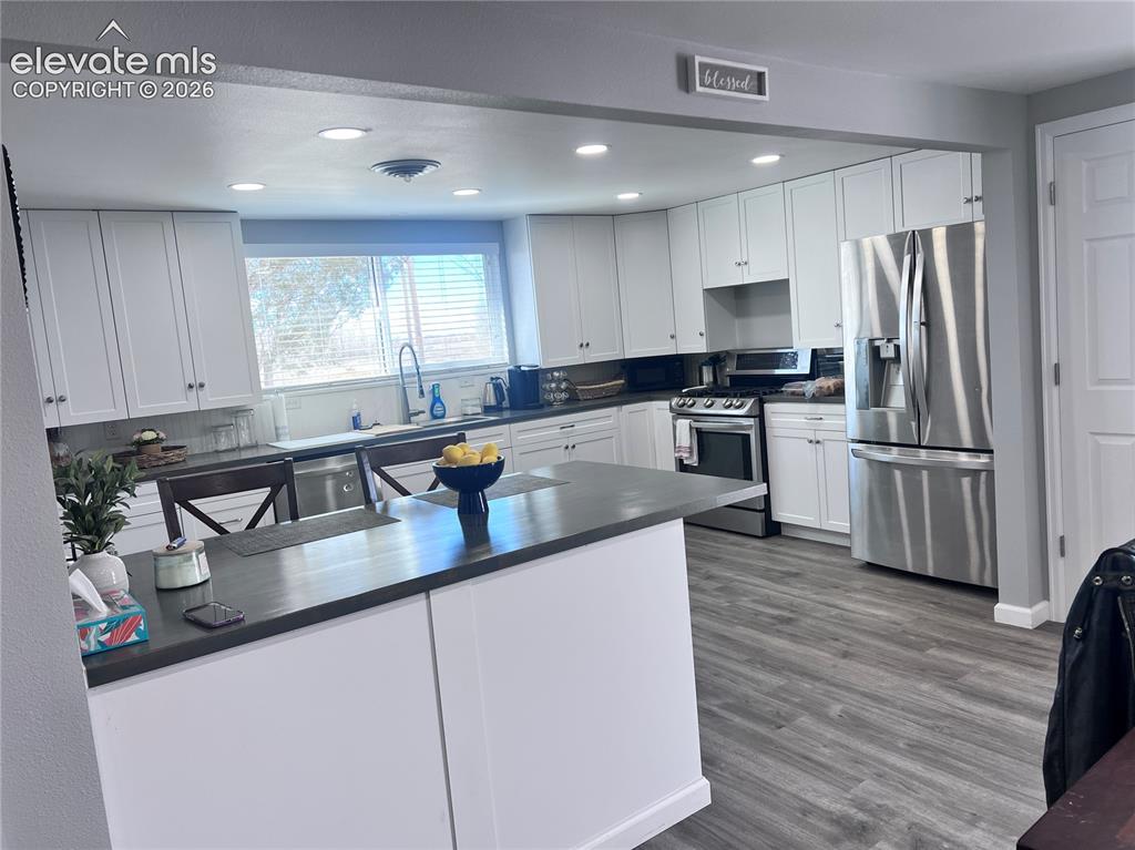 Image 25 of 49: Kitchen featuring white cabinetry, stainless steel appliances, dark counter