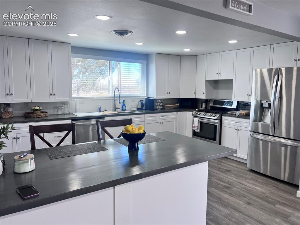 Image 26 of 49: White cabinetry, stainless steel appliances, dark countertops, recessed lig