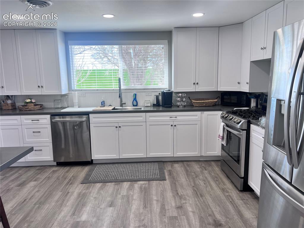 Image 28 of 49: Kitchen featuring white cabinetry, stainless steel appliances, dark counter