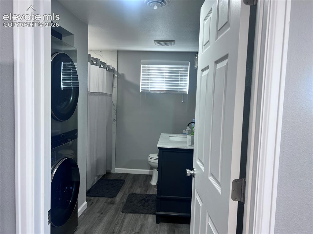 Image 31 of 49: Bathroom with wood-finish flooring, a dark vanity, and a stacked washer and