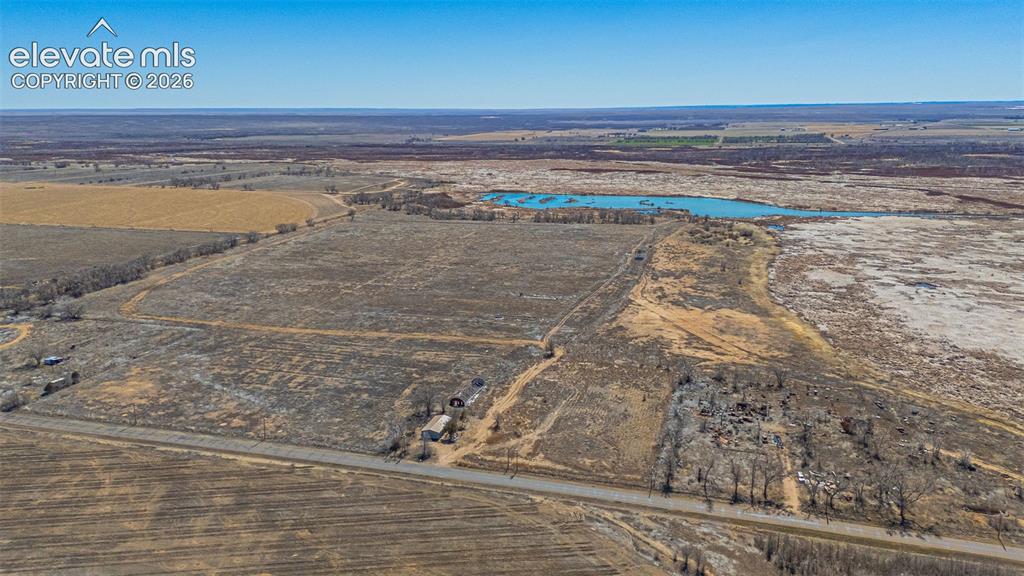 Image 40 of 49: Expansive land parcel featuring open fields, an aquatic body, and a paved r