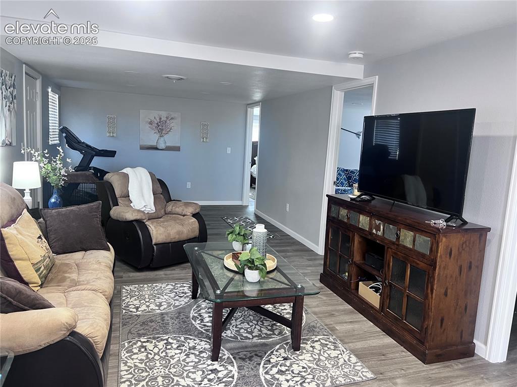 Image 8 of 49: Recessed lighting, wood-finish flooring, and a media console with glass-fro