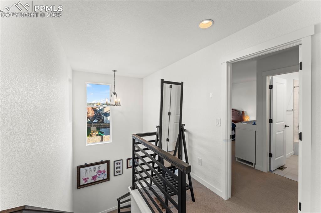 Image 19 of 31: Hall featuring an upstairs landing, a chandelier, a textured wall, light ca