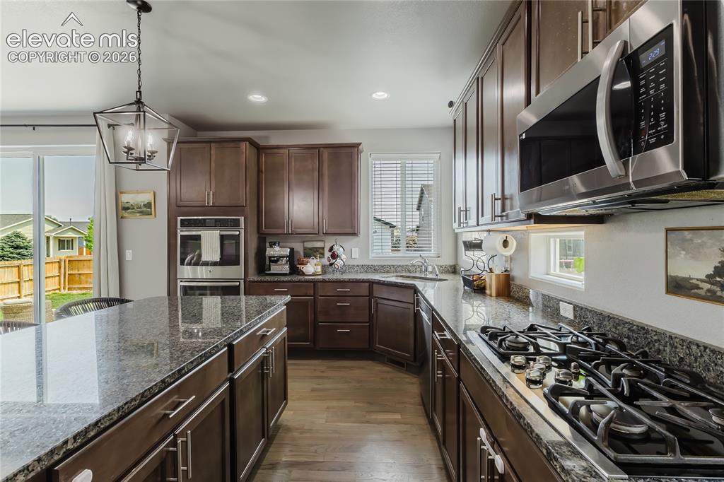 Image 16 of 46: Kitchen featuring dark wood cabinetry, granite countertops, wood-finish flo