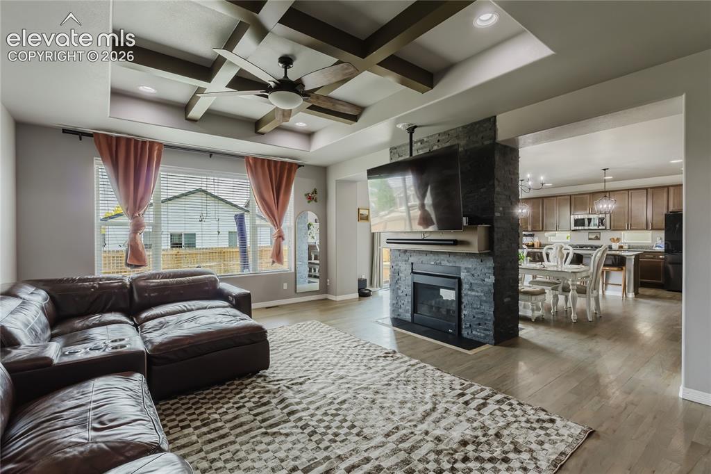 Image 8 of 46: Living area featuring a coffered ceiling with a ceiling fan, a fireplace wi