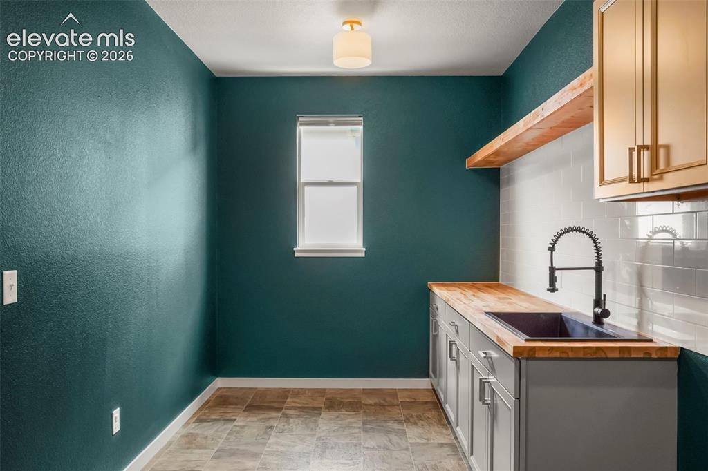 Image 13 of 37: Laundry with sink featuring teal walls, wood-finish countertops, subway til