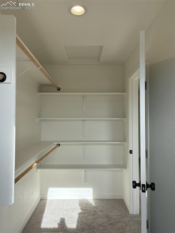 Image 6 of 22: Walk in closet with attic access and light colored carpet